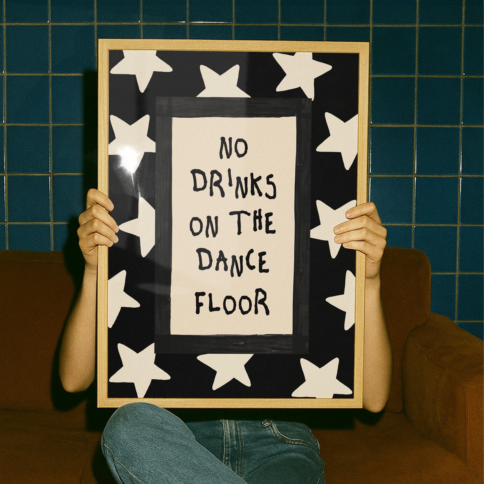 Person holding a framed sign with 'No Drinks on the Dance Floor' text against a blue tiled wall.