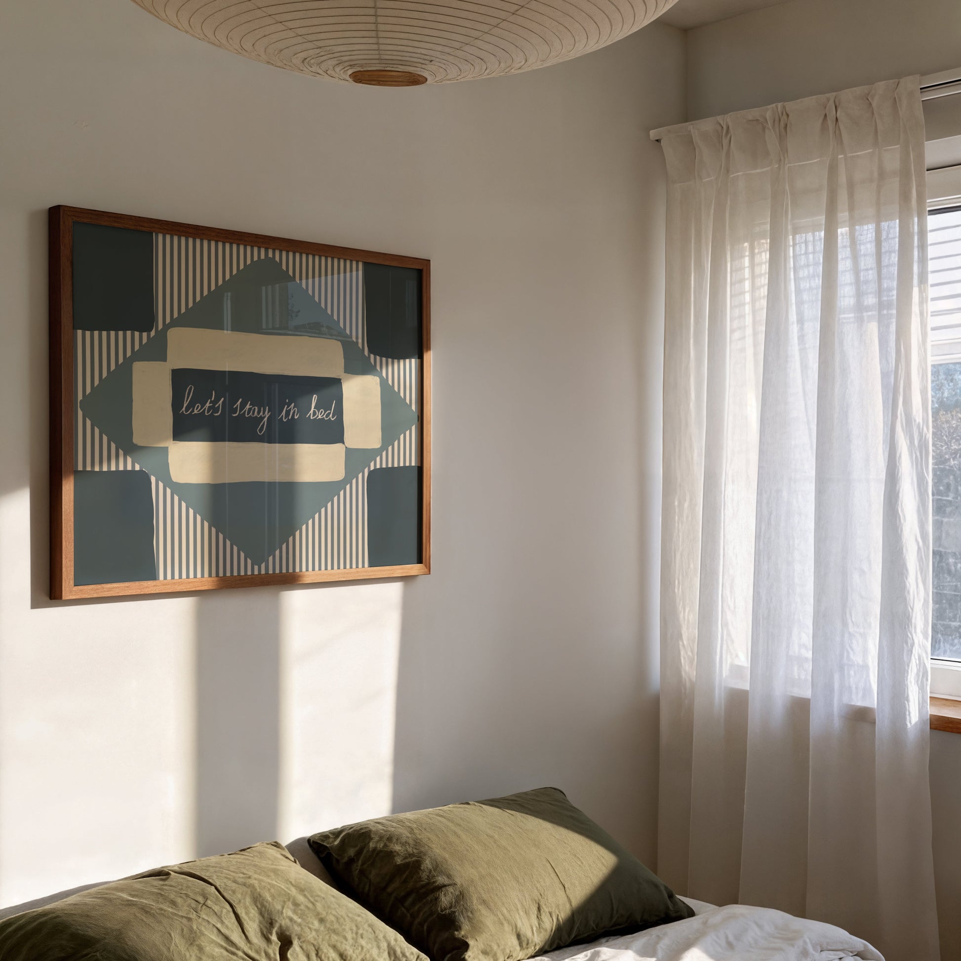 Framed artwork on a wall above a bed with curtains to the side.